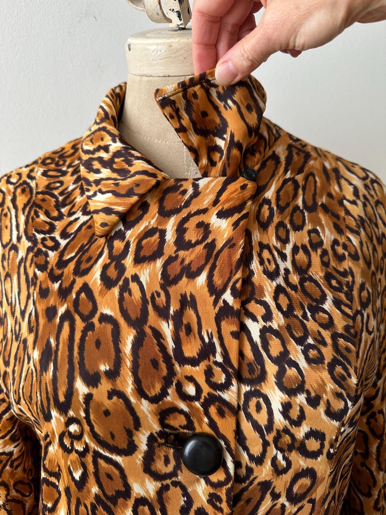 Puede incluir: Chaqueta vintage con estampado de leopardo, cuello cl&aacute;sico y grandes botones negros. La chaqueta presenta un estampado animal marr&oacute;n, beige y negro. La tela parece ser ligera, adecuada para usar en capas.