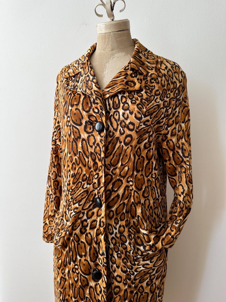 Puede incluir: Un abrigo de manga larga con estampado de leopardo, cuello y grandes botones negros. El abrigo tiene dos bolsillos delanteros y se exhibe en un maniqu&iacute;. El dise&ntilde;o de estampado animal incluye tonos de marr&oacute;n, beige y negro.