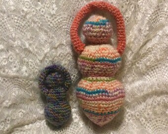 May include: Two crocheted dolls, one with a pink and orange head and a striped body, the other with a purple head and a striped body.