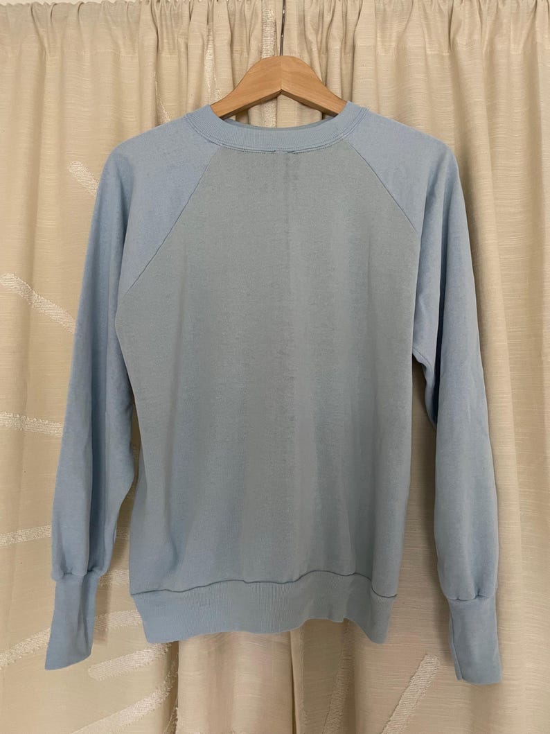 Op de afbeelding: Een lichtblauw sweatshirt met een raglanmouw ontwerp. Het sweatshirt heeft een ronde hals en een geribbelde zoom.