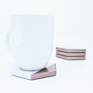 May include: White ceramic mug with a textured surface, sitting on a white and rose gold hexagonal coaster.