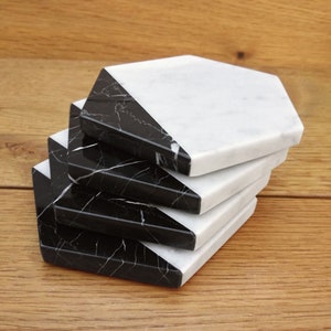 May include: Four black and white marble hexagon coasters stacked on top of each other. The coasters are made of natural stone and have a polished finish.