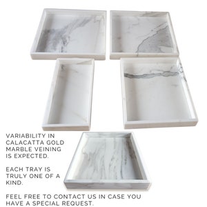 Set of five white marble trays with a gold veining pattern. Each tray is a unique shape and size. Variability in marble veining is expected. Each tray is truly one of a kind. Feel free to contact us in case you have a special request.