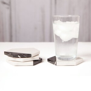May include: Four black and white marble hexagon coasters with a glass of water with ice on a white surface.