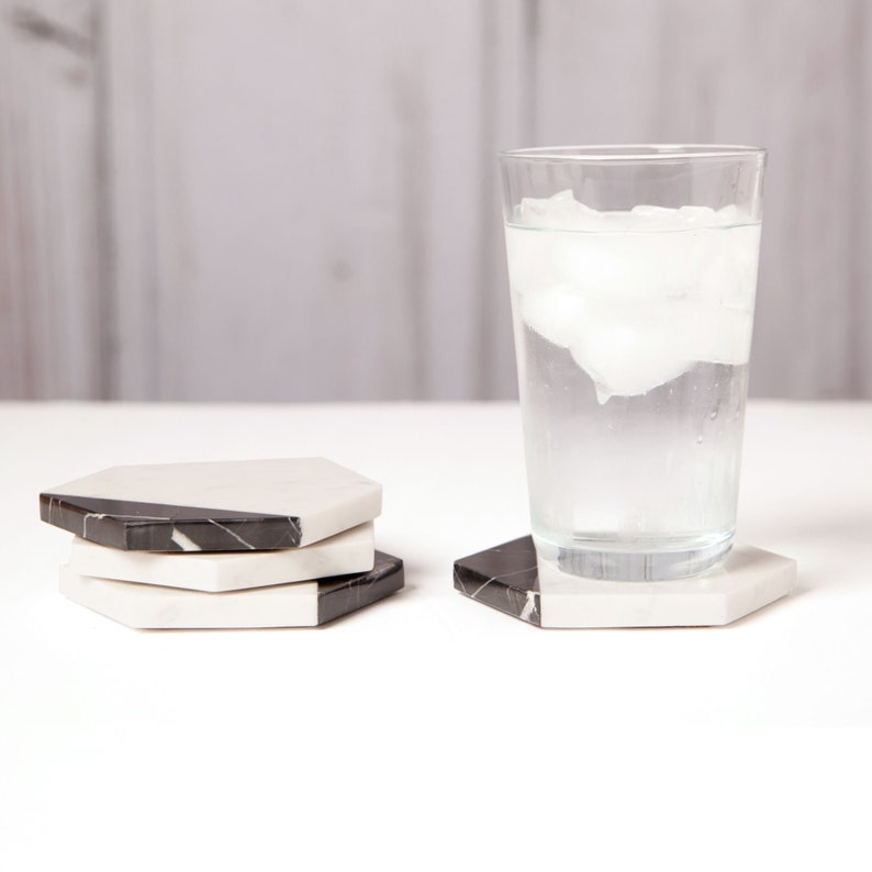 May include: Four black and white marble hexagon coasters with a glass of water with ice on a white surface.
