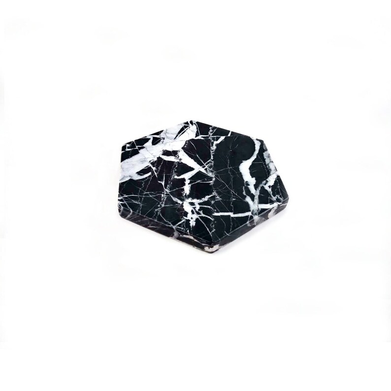 May include: Black and white marble hexagon coaster. The coaster has a swirling pattern of white veins on a black background.