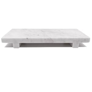 May include: A rectangular white marble serving board with a subtle gray veining pattern. The board is elevated by four small, rectangular feet, giving it a floating appearance. This elegant piece is ideal for serving appetizers or displaying decorative items.