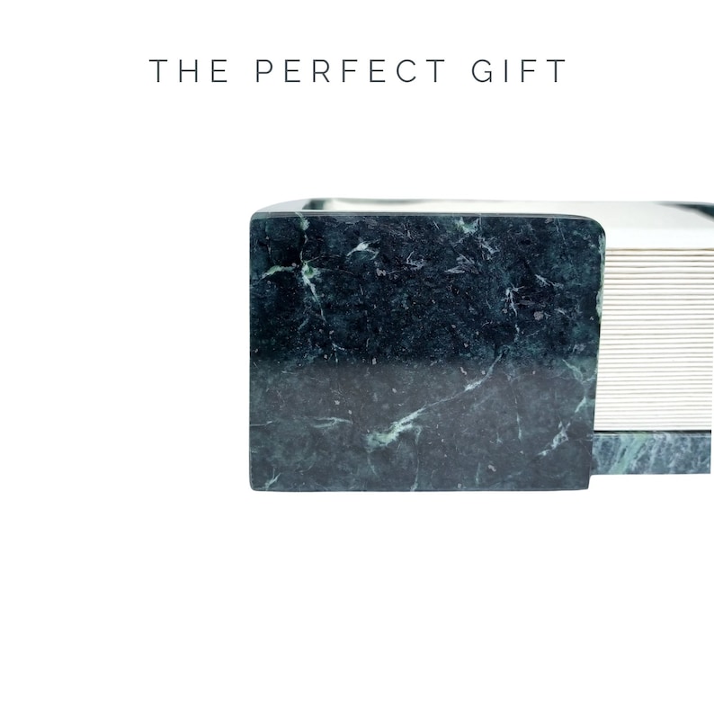 May include: A dark green marble paper holder with white veining, featuring a stack of white paper sheets. The text THE PERFECT GIFT is printed in black above the object. The marble has a polished finish and a rectangular shape.