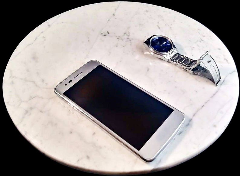 Może przedstawiać: Biały smartfon z czarnym ekranem i srebrny zegarek z niebieską tarczą na białym marmurowym blacie.