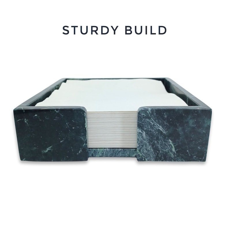 May include: A dark green marble napkin holder with a polished finish and a square shape, containing a stack of white paper napkins. The text STURDY BUILD is printed in dark blue letters above the holder, which features a front cutout.