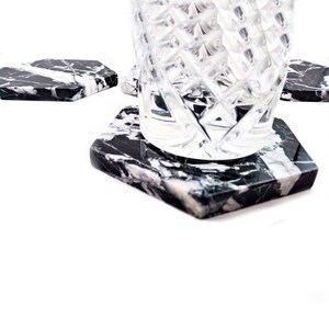 May include: Set of four black and white marble hexagon coasters with a clear glass on top of one coaster.