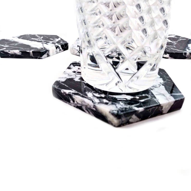 May include: Set of four black and white marble hexagon coasters with a clear glass on top of one coaster.