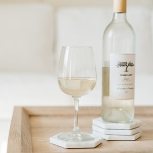 May include: A glass of white wine and a bottle of Trader Joe's Pinot Grigio on a wooden table with white coasters.