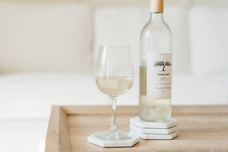 May include: A glass of white wine and a bottle of Trader Joe's Pinot Grigio on a wooden table with white coasters.