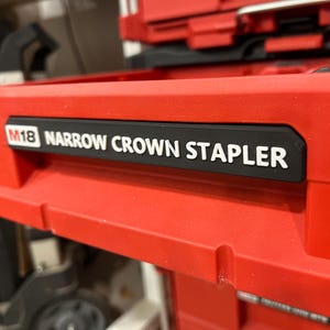 May include: Red power tool case with a black label that reads "M18 NARROW CROWN STAPLER" in white lettering. The tool case is part of a larger set of tools.