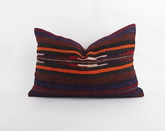 May include: A rectangular throw pillow featuring a woven textile cover with horizontal stripes in shades of dark purple, black, deep red, and bright orange. The fabric displays a textured, coarse appearance with subtle geometric patterns.