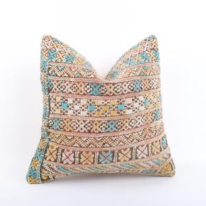 May include: A decorative pillow with a colorful geometric pattern in shades of blue, brown, beige, and white. The pillow is made of woven fabric and has a traditional design.