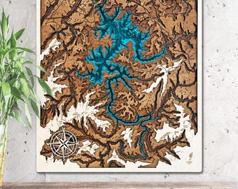 May include: Wooden wall art featuring a detailed topographic map of Lake Blue Ridge, Georgia. The map has a layered design with brown, white, and turquoise blue elements. A compass rose is in the lower left corner, and the text "LAKE BLUE RIDGE Georgia" is at the top.