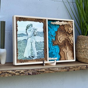 May include: A wooden framed photo and map display. The left side features a photo of a couple embracing. The right side has a layered map design with blue and brown tones, and the text "April 13, 2017".