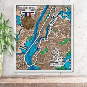 May include: Wooden map art of New York City with a white frame. The map features a layered design with blue water and brown land. Includes a cyclist graphic and text "NEW YORK CITY BIKE TOUR". A medal reads "CYCLING YOUR MEDAL HERE".