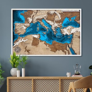 Può includere: Una mappa in legno incorniciata del Mar Mediterraneo, con dettagliati contorni di rilievo e profondità. La mappa utilizza sfumature di marrone, bianco e blu per rappresentare la terra e l'acqua. Il testo "MEDITERRANEAN SEA" è in alto.