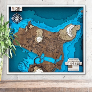 May include: A layered wooden map with a white frame, featuring a detailed topographical design. The map has a brown wooden base with blue water features and a white compass rose. Text includes "MCBH" and "ONCE A MARINE ALWAYS A MARINE SGT. JOHN MILLER".