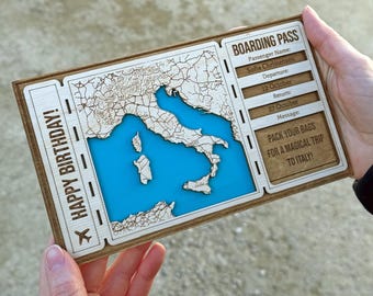 May include: A wooden boarding pass featuring a map of Italy with a blue resin sea. The pass includes the text "HAPPY BIRTHAY!" and "PACK YOUR BAGS FOR A MAGICAL TRIP TO ITALY!" with passenger details and travel dates.