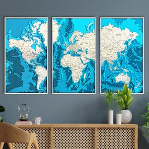 May include: Three framed world map art pieces. Each map features a detailed, layered design with blue ocean depths and beige landmasses. The frames are white, and the overall aesthetic is modern and decorative.