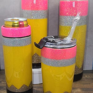 May include: Set of four yellow, pink and silver glitter tumblers with black lids and straws. The tumblers are decorated to look like pencils.