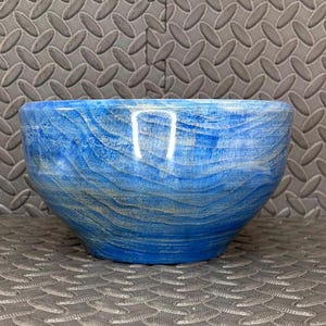 May include: A handcrafted wooden bowl with a vibrant blue finish. The bowl features a natural wood grain pattern and a smooth, rounded shape. The bowl is perfect for serving or as a decorative piece.