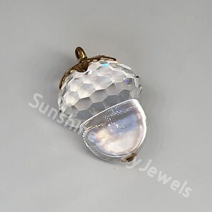 May include: A clear crystal acorn charm with a gold-toned cap. The charm is faceted and has a iridescent finish.