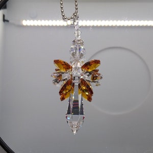 May include: A crystal angel suncatcher with a clear crystal body and amber wings hanging from a silver chain.