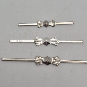 May include: Three silver-toned metal components arranged horizontally, each featuring a central hexagonal shape with radiating fan-like textures on either side, extending into thin, straight, flat bars on both ends of the piece.
