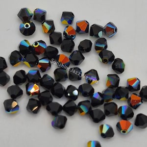 May include: A collection of faceted black beads with iridescent color flashes of orange, yellow, and blue. The beads are scattered on a white surface. The beads are likely for jewelry making.