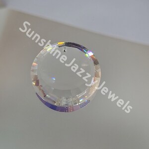 May include: A clear crystal pendant with a faceted design and a hole at the top for hanging. The pendant is round and has a rainbow iridescent sheen.