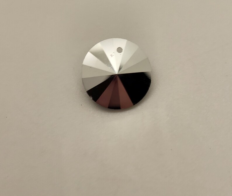 以下が含まれることがあります： 上部に紐を通すための穴のある、銀色のファセット加工が施された楕円形のペンダント