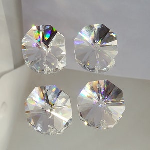 May include: Four clear crystal octagon shaped prisms with iridescent rainbow facets. The prisms have a hole in the center for hanging.