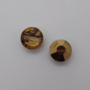 May include: Two round, gold-toned glass beads. One bead is clear with a faceted design, and the other bead is amber with a textured surface.