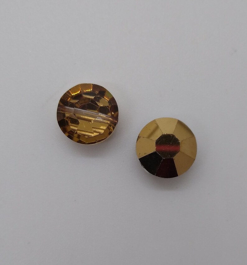 May include: Two round, gold-toned glass beads. One bead is clear with a faceted design, and the other bead is amber with a textured surface.