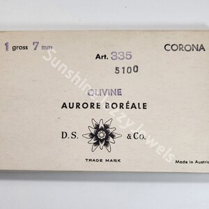 K&ouml;nnte beinhalten: Eine wei&szlig;e Schachtel mit schwarzem Text, der "CORONA Art. 335 5100 OLIVINE AURORE BOR&Eacute;ALE D.S. TRADE MARK & Co. Made in Austria" lautet. Die Schachtel enth&auml;lt auch ein Schwarzwei&szlig;bild einer Blume.