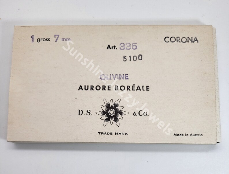 K&ouml;nnte beinhalten: Eine wei&szlig;e Schachtel mit schwarzem Text, der "CORONA Art. 335 5100 OLIVINE AURORE BOR&Eacute;ALE D.S. TRADE MARK & Co. Made in Austria" lautet. Die Schachtel enth&auml;lt auch ein Schwarzwei&szlig;bild einer Blume.