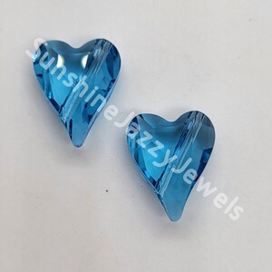 May include: Two light blue crystal heart-shaped beads with a hole through the center. The beads are on a white background.