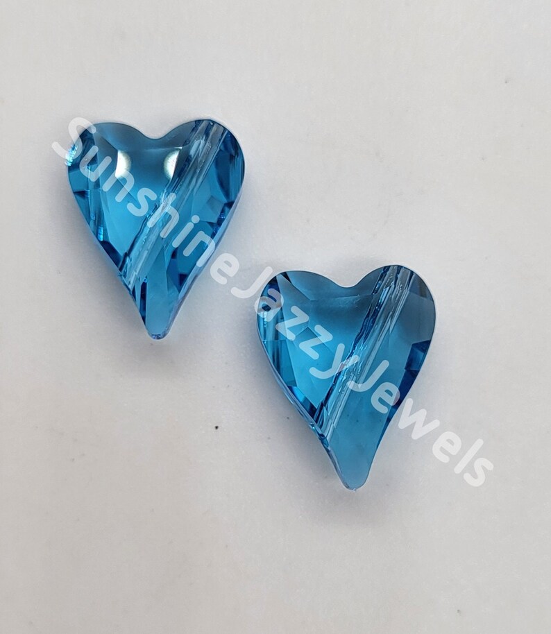 May include: Two light blue crystal heart-shaped beads with a hole through the center. The beads are on a white background.