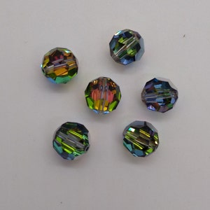 May include: Six iridescent glass beads with a faceted design. The beads are green, blue, and gold in color.