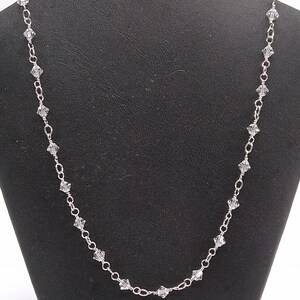 May include: A silver chain necklace with clear crystal beads. The necklace is displayed on a black velvet background.