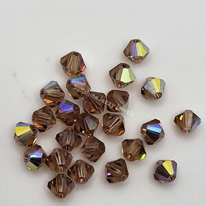 May include: A collection of faceted, brown crystal beads with iridescent color shifts. The beads are scattered on a white surface. The text "Sunshine Jazzy Jewels" is visible in the image.