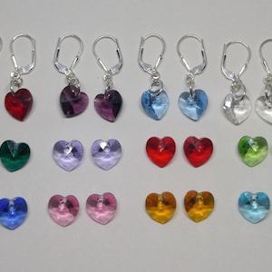 May include: A set of 12 pairs of silver heart-shaped earrings with crystal accents. The earrings come in a variety of colors, including red, purple, blue, green, pink, and orange.