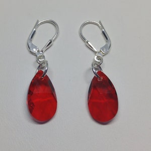 May include: A pair of silver dangle earrings with red teardrop-shaped crystal stones.