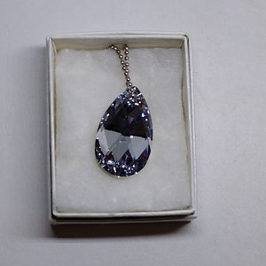 May include: A clear teardrop-shaped crystal pendant necklace with a silver chain in a white box.