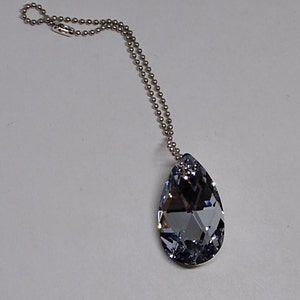 May include: A silver chain necklace with a teardrop-shaped crystal pendant. The crystal is clear with a slight blue tint.